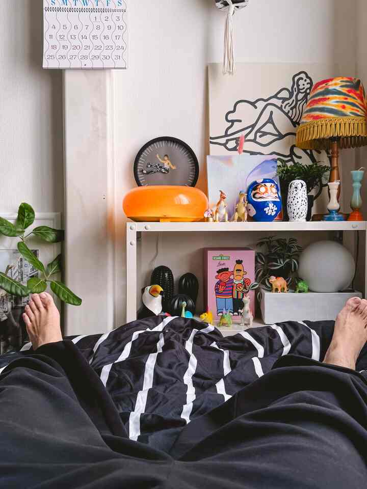 Black and white toned bedroom featuring a bed with striped bedding, colorful decorative objects, and a tie-dye pattern table lamp creating a cozy vibe