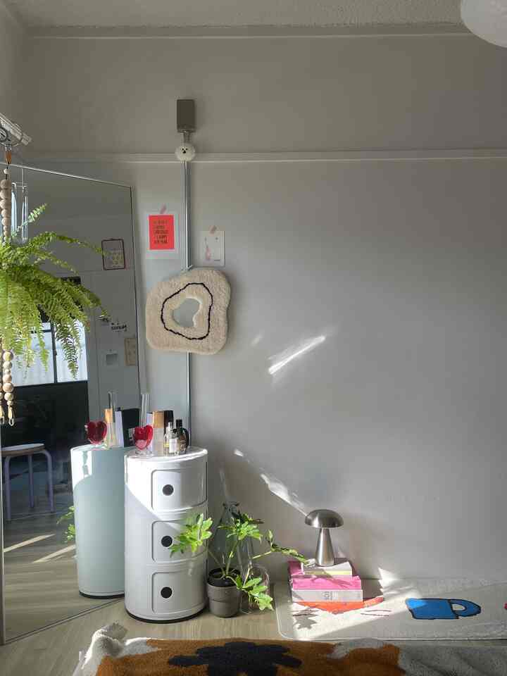 柔らかなホワイトとナチュラルカラーのリビング、丸い収納キャビネットとミッドセンチュリーモダンスタイルのシルバーランプ、植物が調和した居心地の良い空間