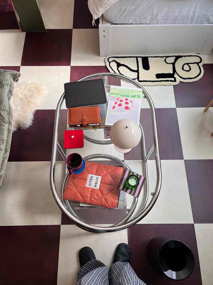 透明なガラステーブルと床のタイルが印象的な、白いベッドがあるフレンチカントリーのリビングスペース