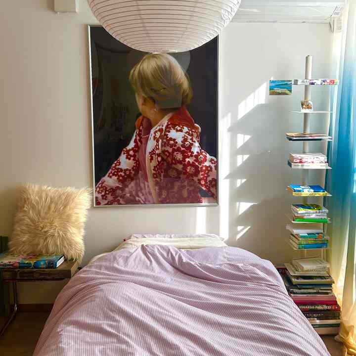 明るくナチュラルな色調の寝室、中央にピンクの寝具が置かれたベッドと右側に本棚が配された雰囲気のあるインテリア