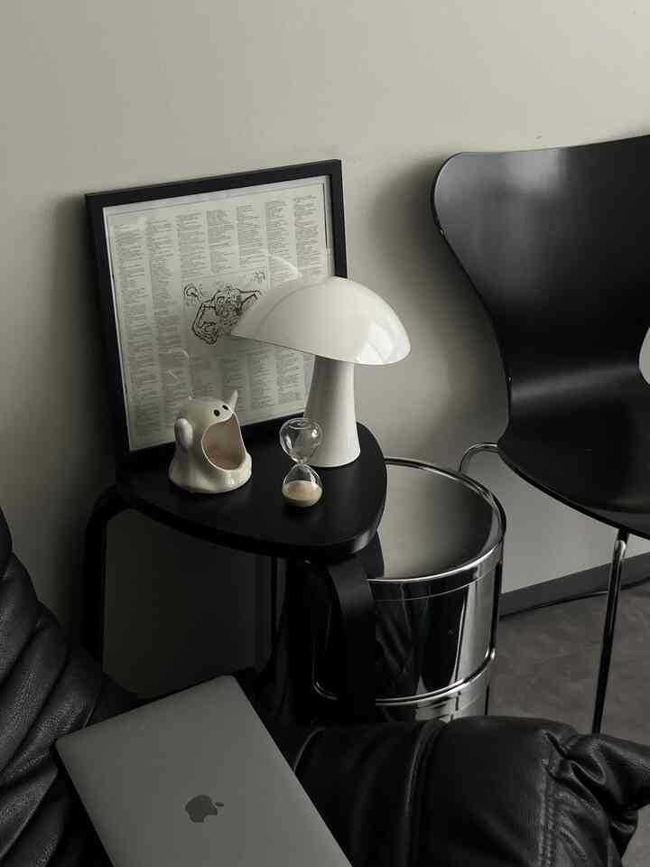 Monotone and silver toned living room corner featuring black leather armchair, silver stool, and white mushroom lamp in a simple setting