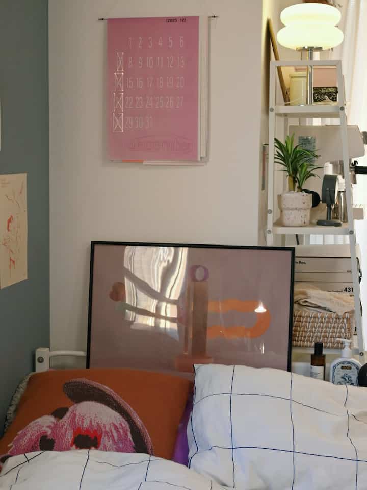 白を基調とした寝室、パターンの掛け布団カバーとポスター、クッションが配置された雰囲気のある空間