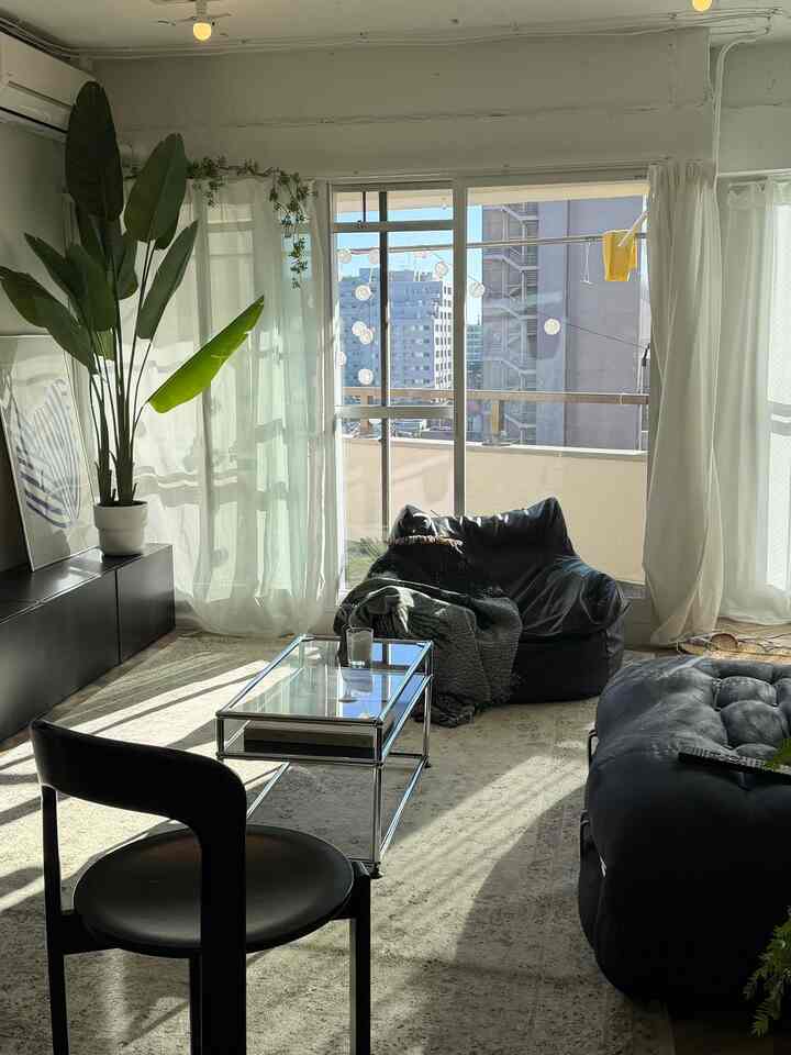 明るい自然光が差し込む白と黒のトーンのリビング、黒いビーズクッションとガラスのコーヒーテーブルが配置されたモダンな雰囲気の空間