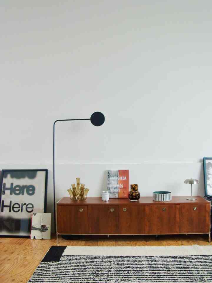 白い壁と木目調のテレビ台、フロアランプとポスターが配置されたミッドセンチュリーモダンのリビングルーム