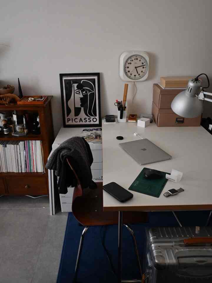 白を基調とした書斎空間、ミッドセンチュリーモダンの机と椅子、壁掛け時計と作業灯が配置された落ち着いたインテリア