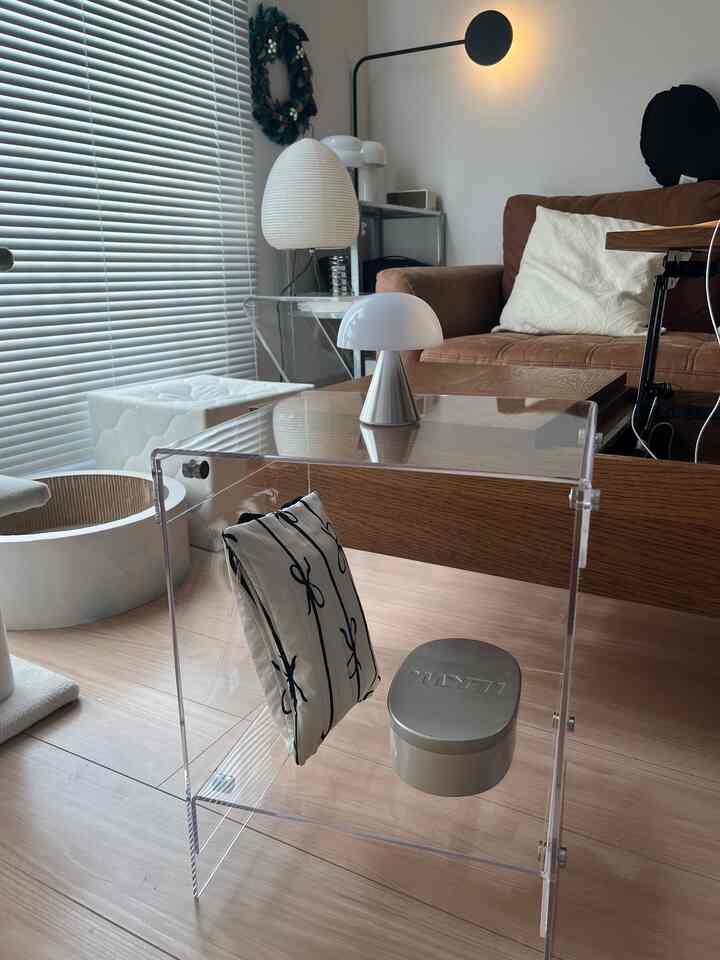 透明なアクリルのサイドテーブルとブラウンのソファが配置された明るく自然な雰囲気の寝室空間