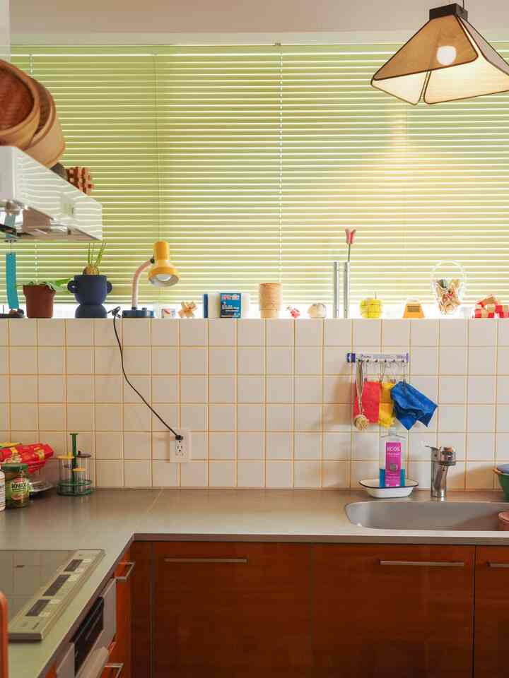 Compact kitchen featuring light gray tiles and warm wood tone cabinets, highlighted by pale green blinds and pendant lighting
