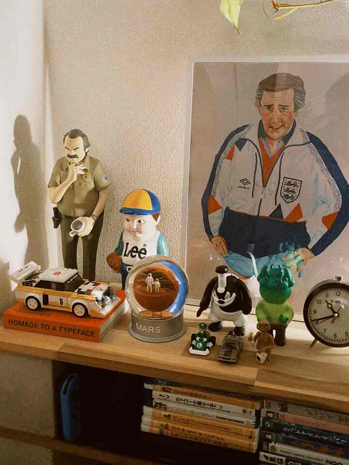 暖かいブラウンウッド調のリビング、ミッドセンチュリーモダンスタイルのフィギュアと時計を配した本棚がある印象的なインテリア