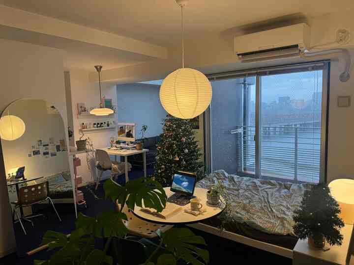 A cozy studio bedroom featuring blue carpet and white walls, with a desk, bed, and decorated Christmas tree arranged inside