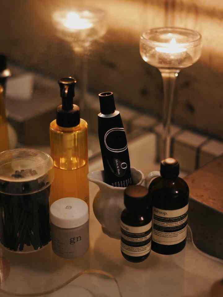 Warm brown and white toned bathroom vanity featuring assorted skincare products and a lit candle creating a cozy atmosphere