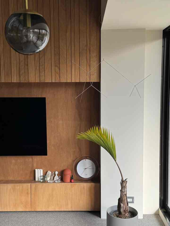 ナチュラルな木目調の壁とグレーのカーペットがあるリビング、 大きな観葉植物とモビールが配置された落ち着いた雰囲気のインテリア