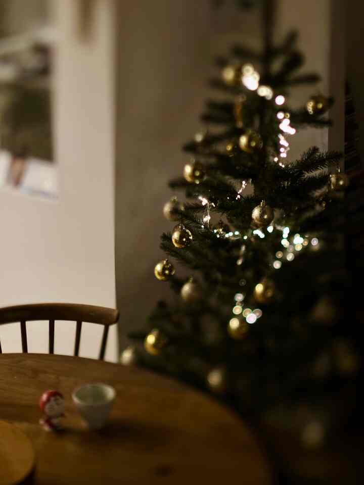 ゴールドとシルバーの飾りが付いたクリスマスツリーと木製のダイニングテーブルが配置された温かみのあるダイニングインテリア