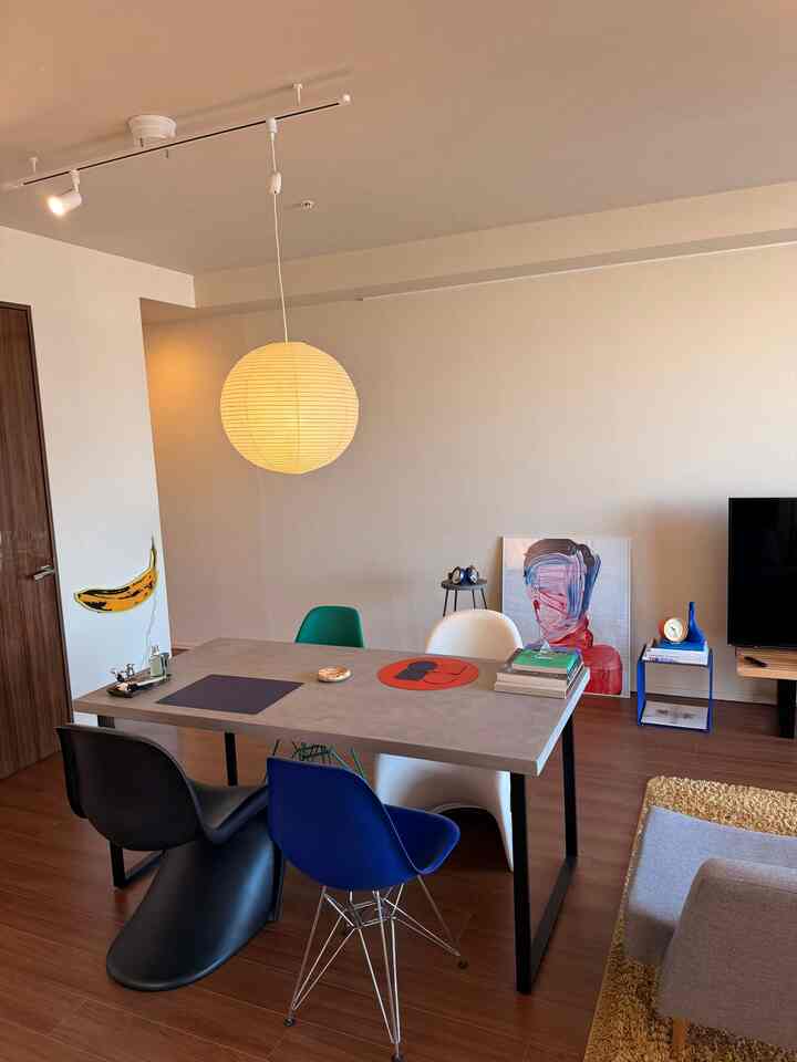 Gray and brown toned studio apartment living and dining area featuring colorful dining chairs and a round pendant light with modern decor