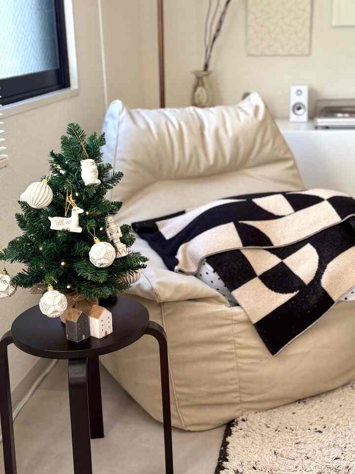 ベージュと黒を基調とした二人暮らしのリビングにビーズクッションチェアと小さなクリスマスツリーが配置された雰囲気のある空間