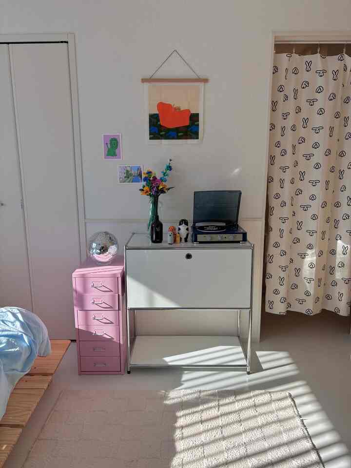 白を基調とした寝室、ピンクの収納キャビネットとレトロなレコードプレーヤーが配置された雰囲気のある空間