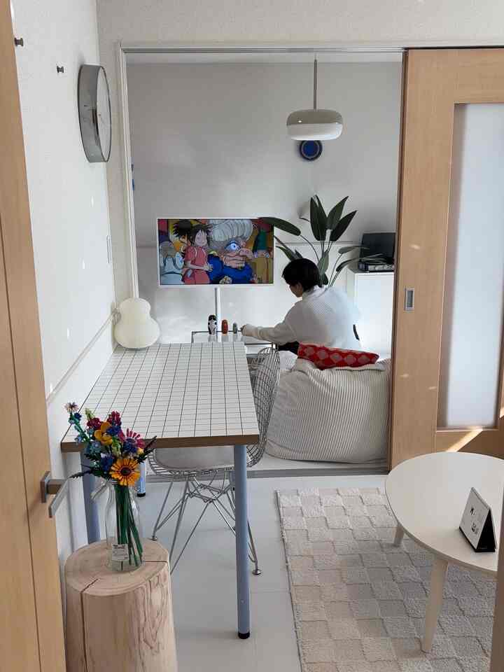 White and natural wood tone studio living room featuring a bean bag sofa, dining table, and TV in a neat compact space