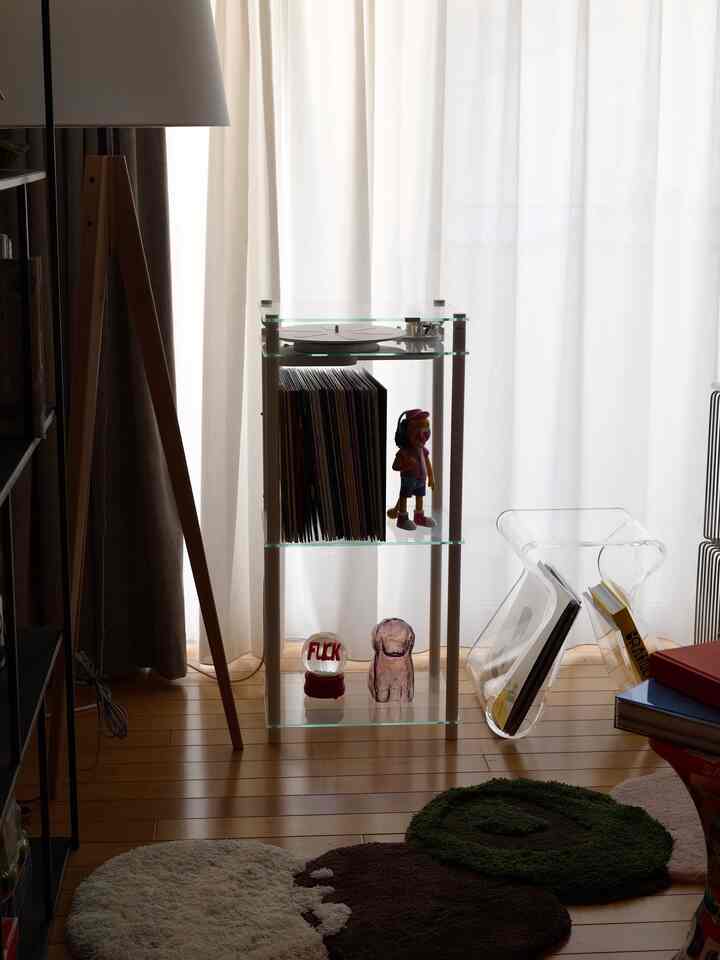 柔らかな自然光が溢れる1LDKのリビング、木目調の床と透明なスツール、ターンテーブルスタンドが配された雰囲気のあるインテリア