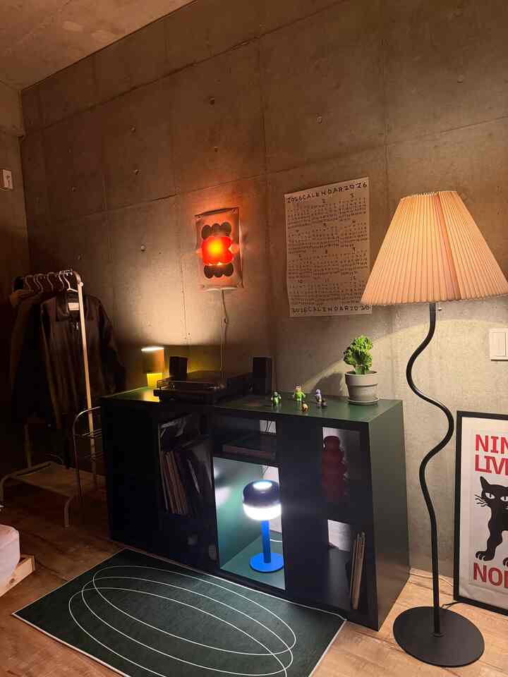 コンクリートの壁と黒いラック、多様な照明とポスターが配置された居心地の良いインダストリアルスタイルのリビングルーム