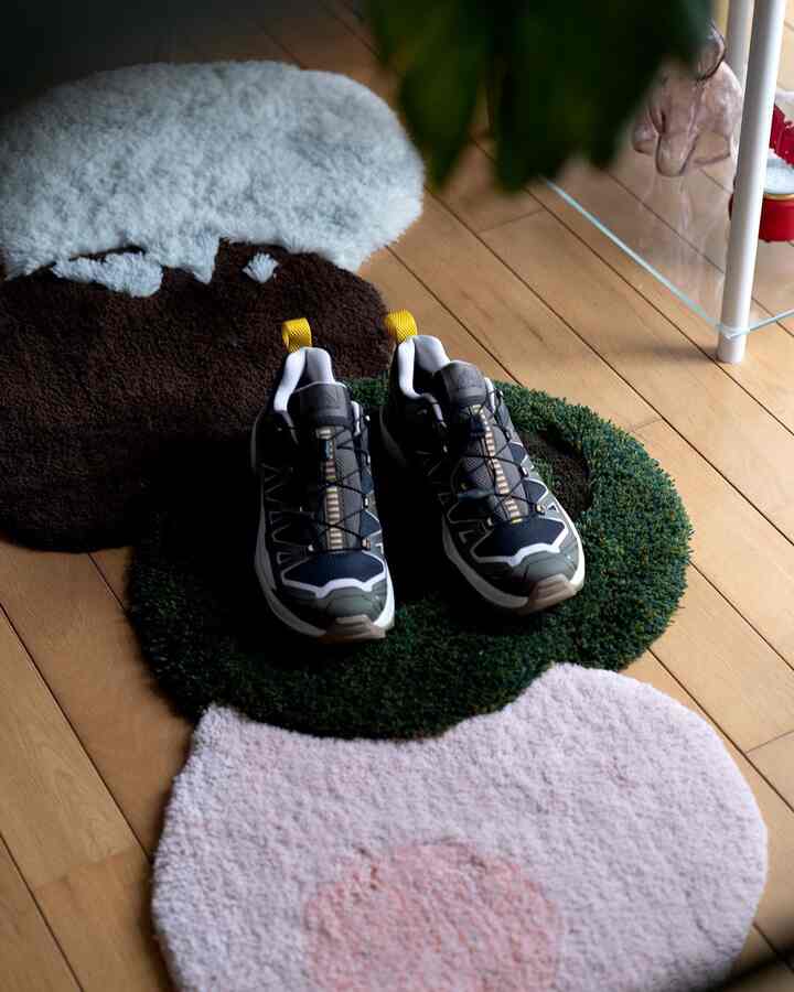 ウッドトーンの床に多色のラグが敷かれ、黒と黄色のアクセントがあるスニーカーが置かれた一人暮らしの空間