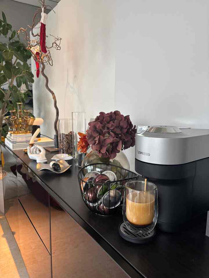 黒とシルバーの家電が配置された洗練されたおうちカフェ空間、花瓶とコーヒーカプセルが飾られたモダンなインテリア