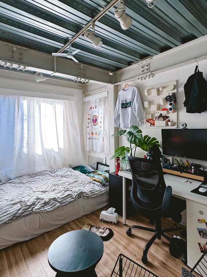 Small studio bedroom with dominant white and wood tones, featuring a desk and office chair in a modern remote work setup