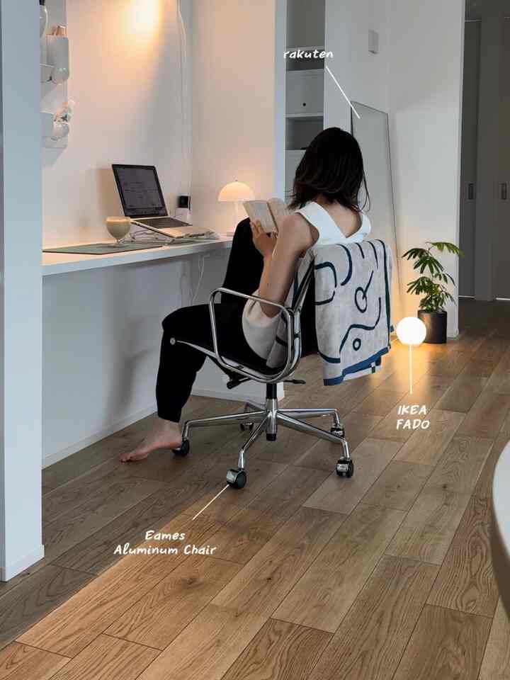 白い壁と木目調床のコンパクトなホームオフィス、イームズアルミニウムチェアとテーブルランプが配置されたモダンで落ち着いた空間