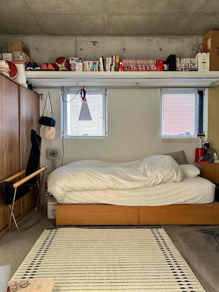 Beige and white toned studio bedroom featuring wooden bed with white bedding and patterned rug in front, creating a cozy atmosphere