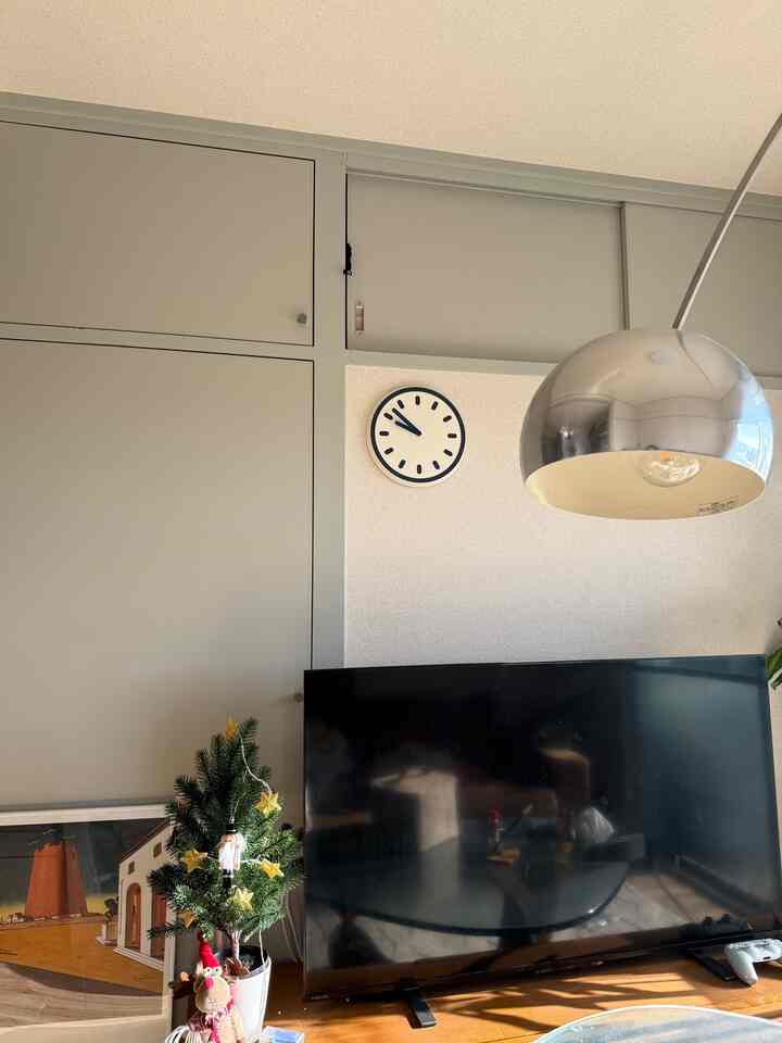 白い壁とネイビーの時計があるリビング、シルバーのランプとテレビが配置された雰囲気の良い空間