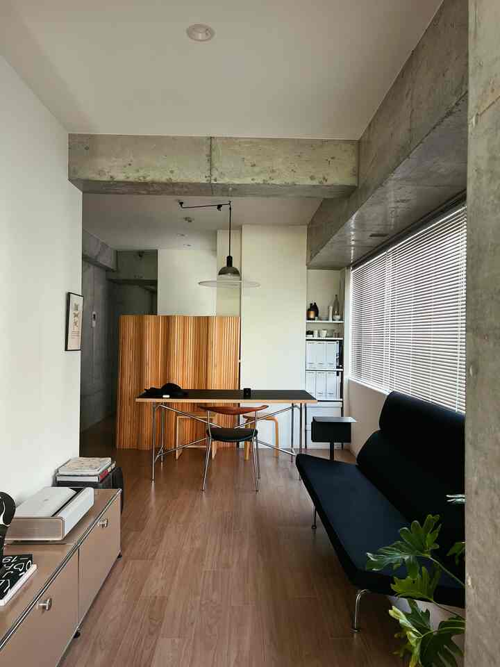 ウッドトーンとブラックが調和した細長いナチュラルモダンなリビング、ソファとダイニングテーブル、間仕切りが配置された印象的な空間