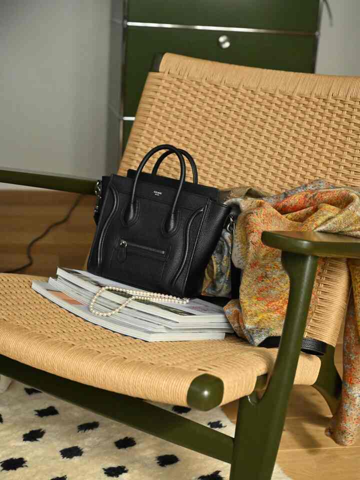 A cozy Nordic living room with natural brown and green tones featuring a CH25 armchair adorned with a small black handbag and colorful blanket