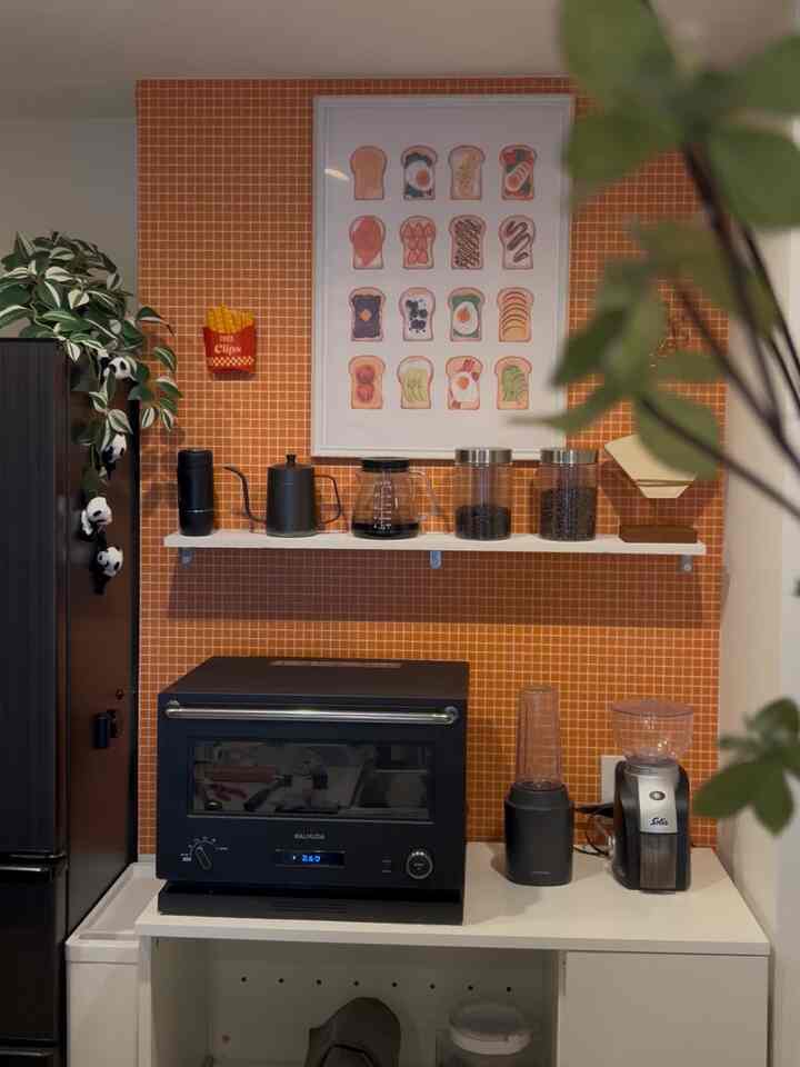 レトロなオレンジタイル壁のキッチン、コーヒー用品と家電が整然と配置された印象的な空間