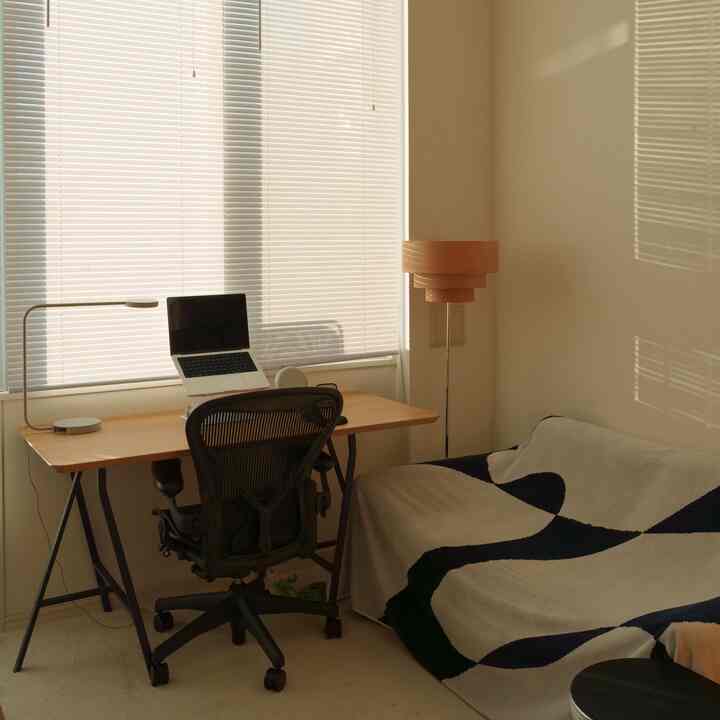 白い壁と木目調のデスク、エアロンチェアが配置されたミニマルでナチュラルなホームオフィスのインテリア