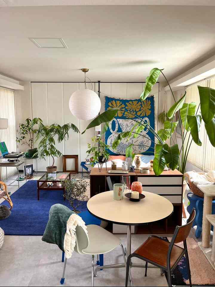 ナチュラルトーンのリビング兼書斎、ミッドセンチュリーモダンの丸テーブルと大きな植物が配置された雰囲気のあるインテリア