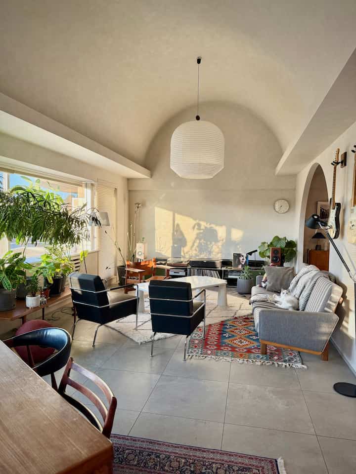 A white and gray toned living room featuring mid-century modern furniture and various plants in a cozy atmosphere