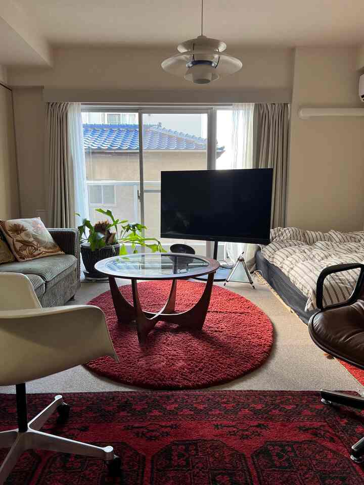 赤いラグとミッドセンチュリーモダン家具のあるワンルーム、ソファとベッドが配置された暖かみのある空間