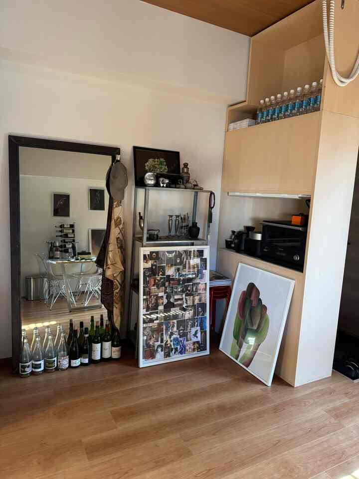 木目調の床と白い壁の1LDK一人暮らし空間、多彩な絵画と大きな鏡が配置された雰囲気のあるインテリア