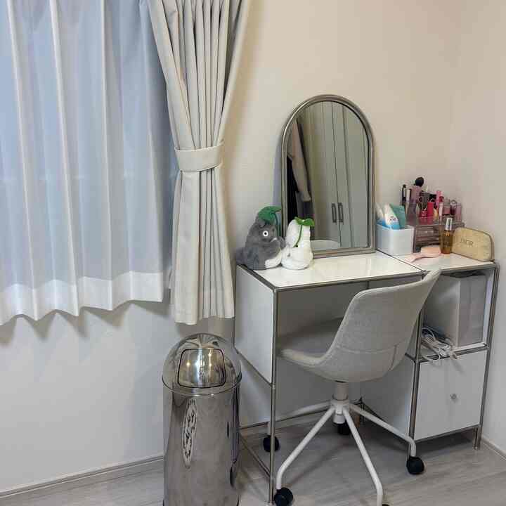 A modern makeup space in a small room featuring a white and silver vanity with mirror and a metallic silver trash bin, neat and minimalistic
