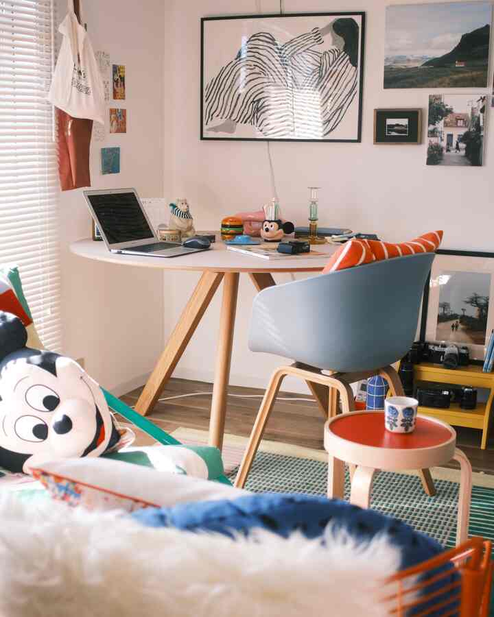 White-walled compact home office featuring a wooden table and chair with colorful posters on the wall