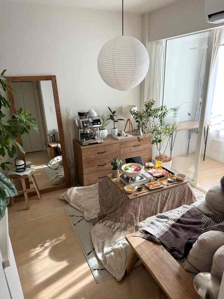 Bright natural-toned living room featuring a kotatsu-style coffee table, sofa, plants, and a large mirror creating a cozy atmosphere