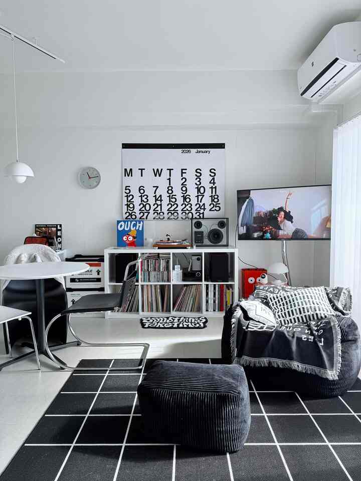 A minimal living room in white and black tones featuring a bean bag sofa and a neatly organized multi-purpose shelf