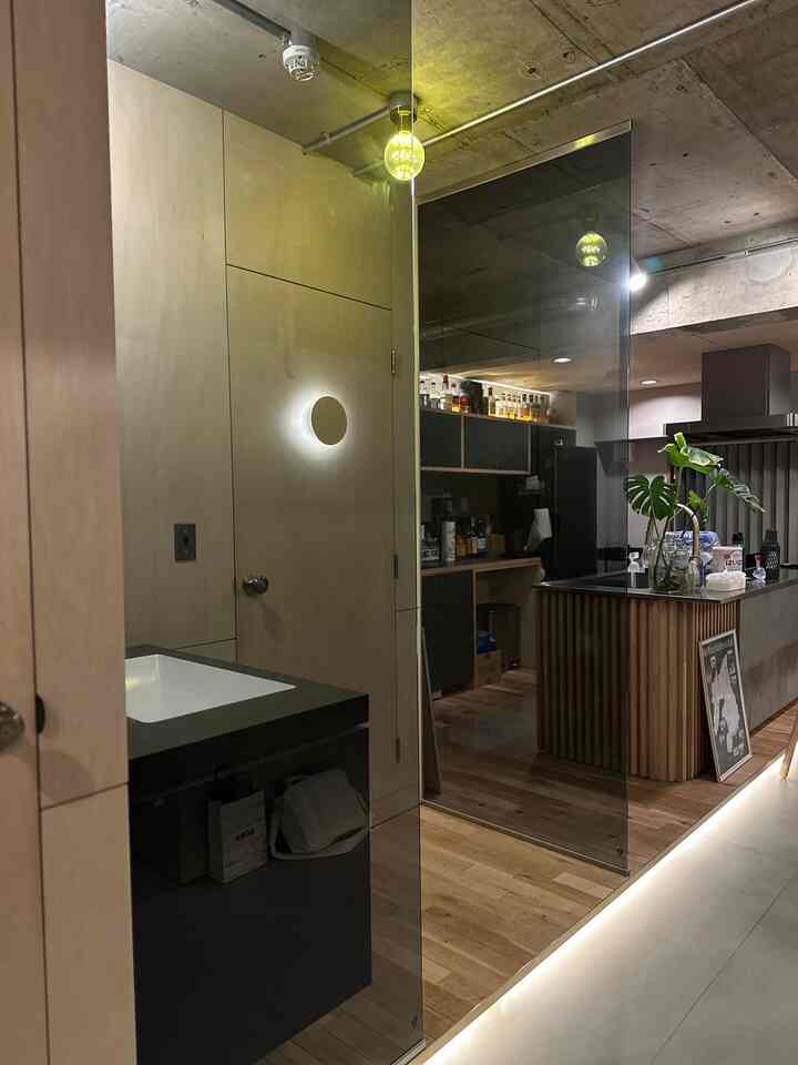 ベージュの壁と木目調の床が調和するバスルームとキッチンの空間、エジソン電球と壁付け照明が雰囲気を演出するモダンなインテリア