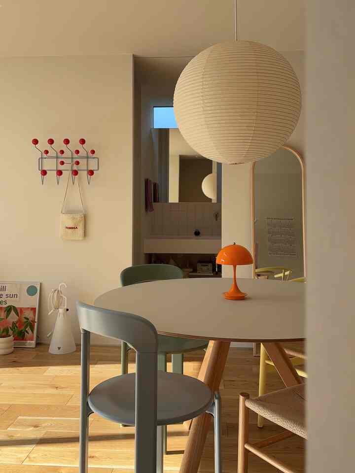 ナチュラルな木目調の床と白い壁のダイニング、中央には丸テーブルとカラフルな椅子、オレンジのテーブルランプが配置された印象的な空間