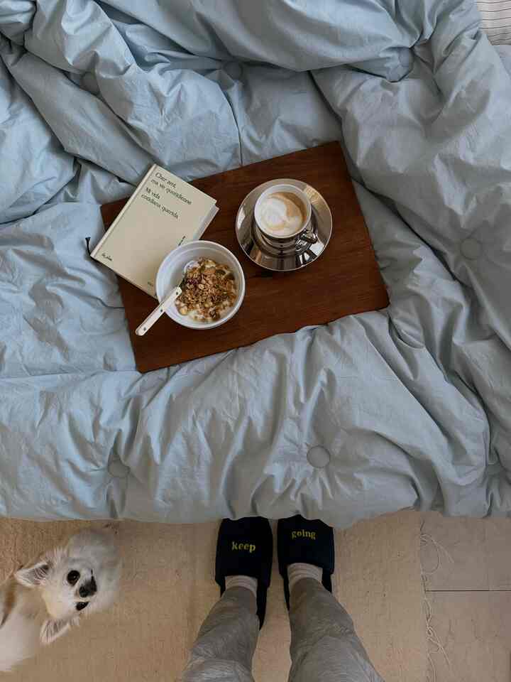 Cozy bedroom with soft pastel blue bedding and a brown wooden tray featuring coffee and cereal