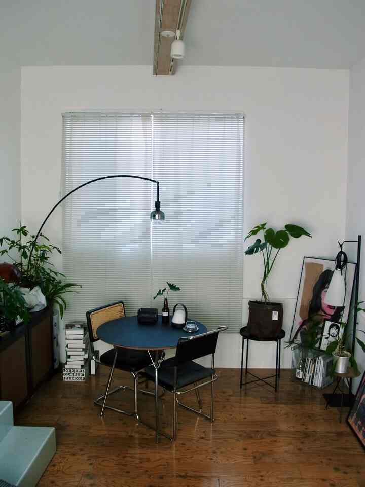 白い壁と木製の床が特徴の北欧風リビング、ブルーのダイニングテーブルと観葉植物、ミッドセンチュリーモダンのフロアランプが配置されたシンプルでモダンなインテリア