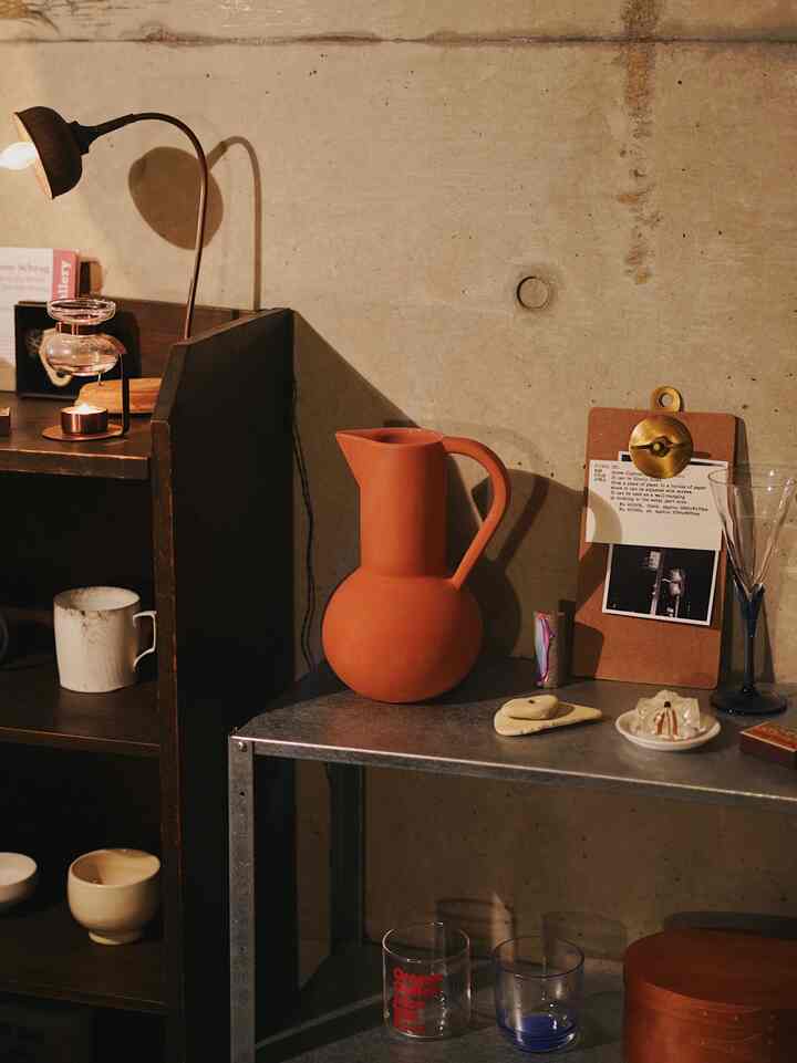 暖かいナチュラルカラーの空間、コンクリート壁と木製の棚、テーブルの上にはテラコッタの花瓶と温かな照明が配置されたインテリア