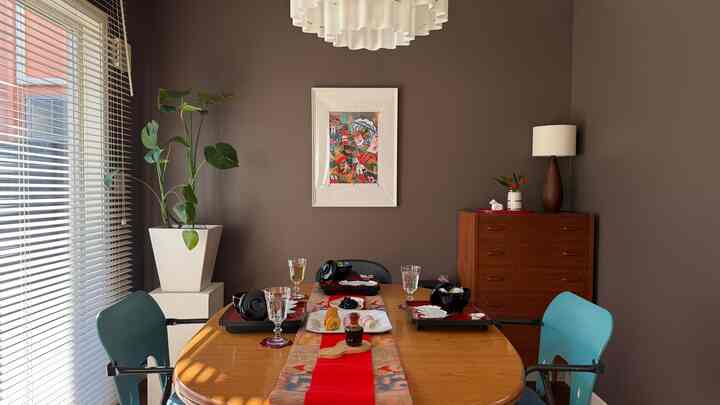 ブラウンの壁と木製ダイニングテーブルが配置されたダイニングルーム、青い椅子と赤いテーブルランナーが雰囲気を演出