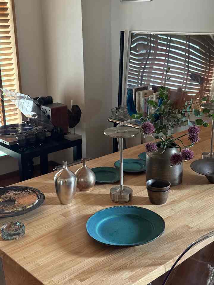 木目調のダイニングテーブルに、シルバーのオブジェと青緑の皿、紫の花瓶が配置された落ち着いた一人暮らし空間