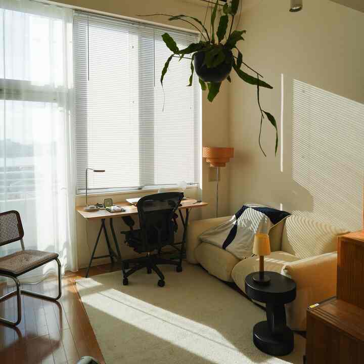 白とベージュのナチュラルな色調のリビング、大きな窓際にデスクとオフィスチェアが配置された明るい空間