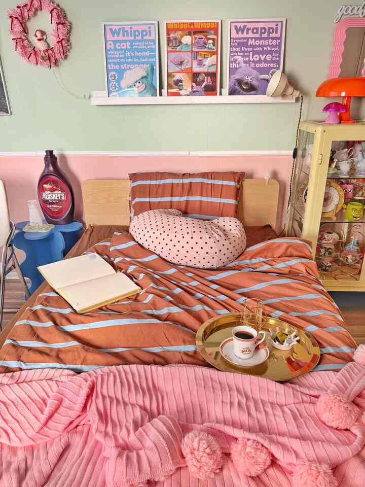 ブラウンとピンクが調和した一人暮らしの寝室、居心地の良いベッドと壁の飾りが配置された雰囲気のあるインテリア