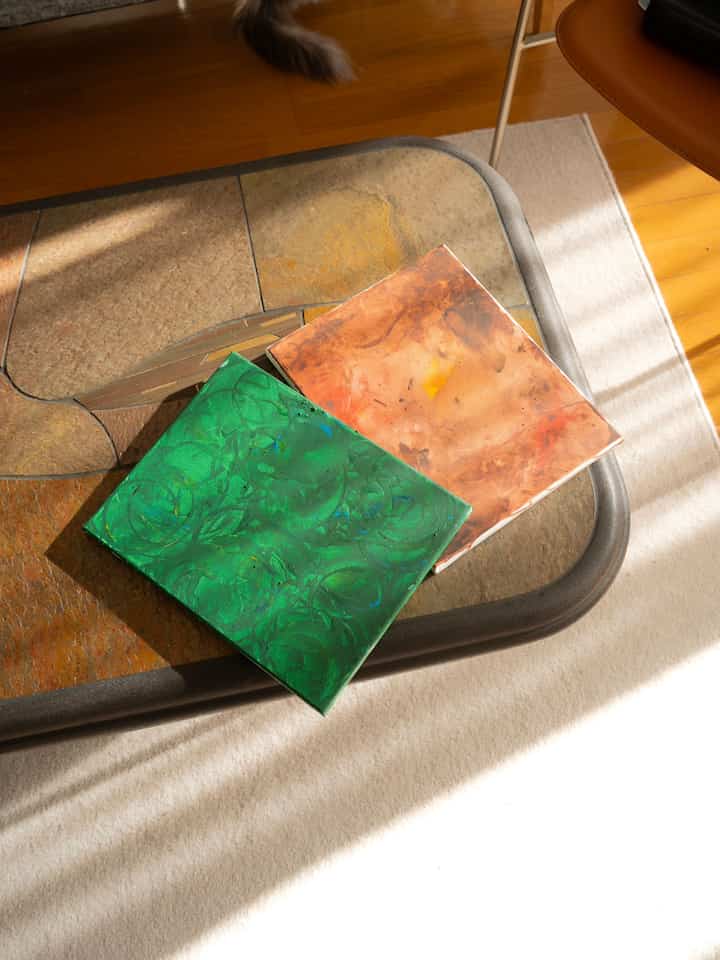 ナチュラルカラーの木製フロアと石のコーヒーテーブル、玄関スペースに緑とオレンジのアクリル画が描かれたキャンバスが置かれた雰囲気のあるインテリア